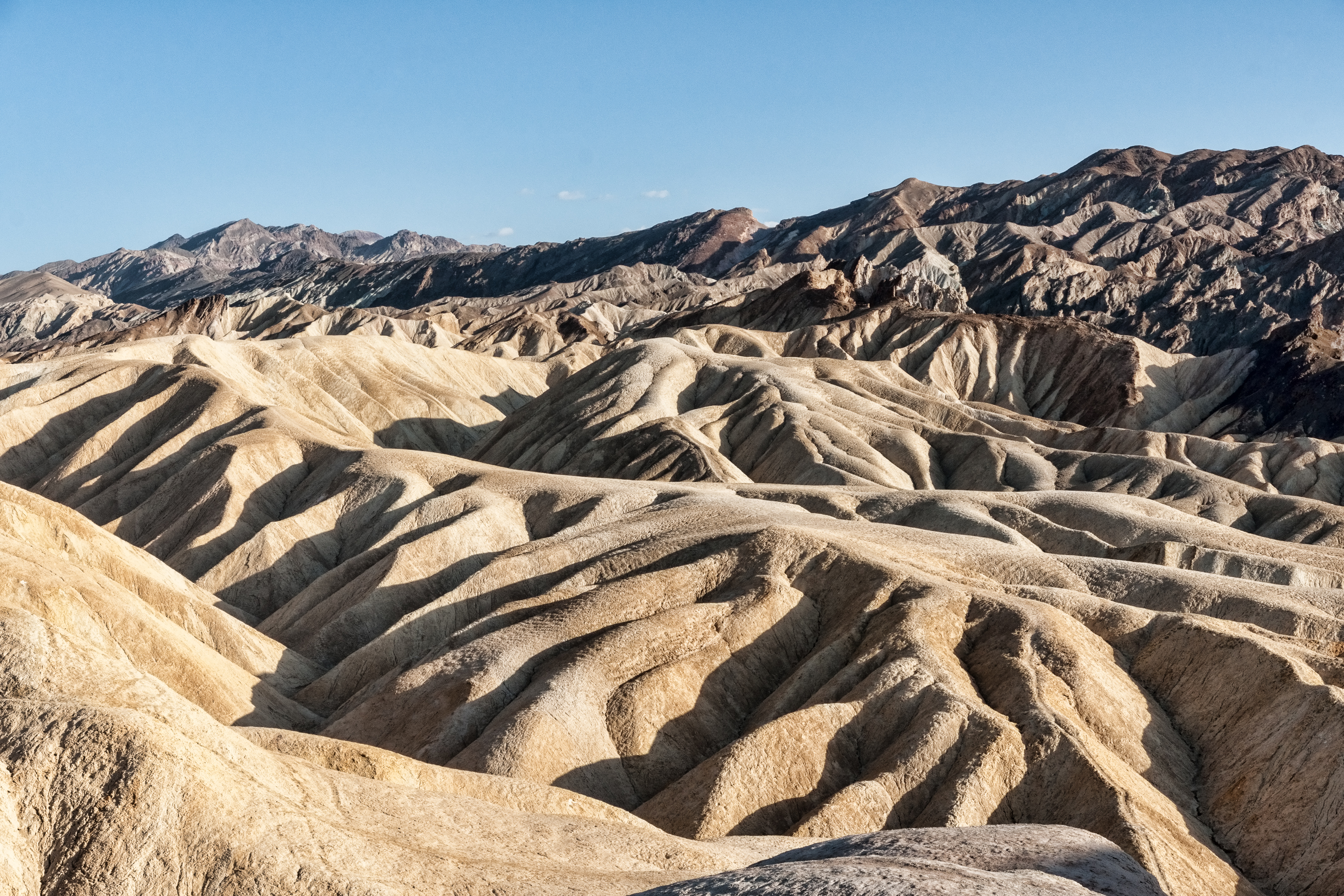 Sunlit folded badlands at Zabriskie Point beneath a clear sky.