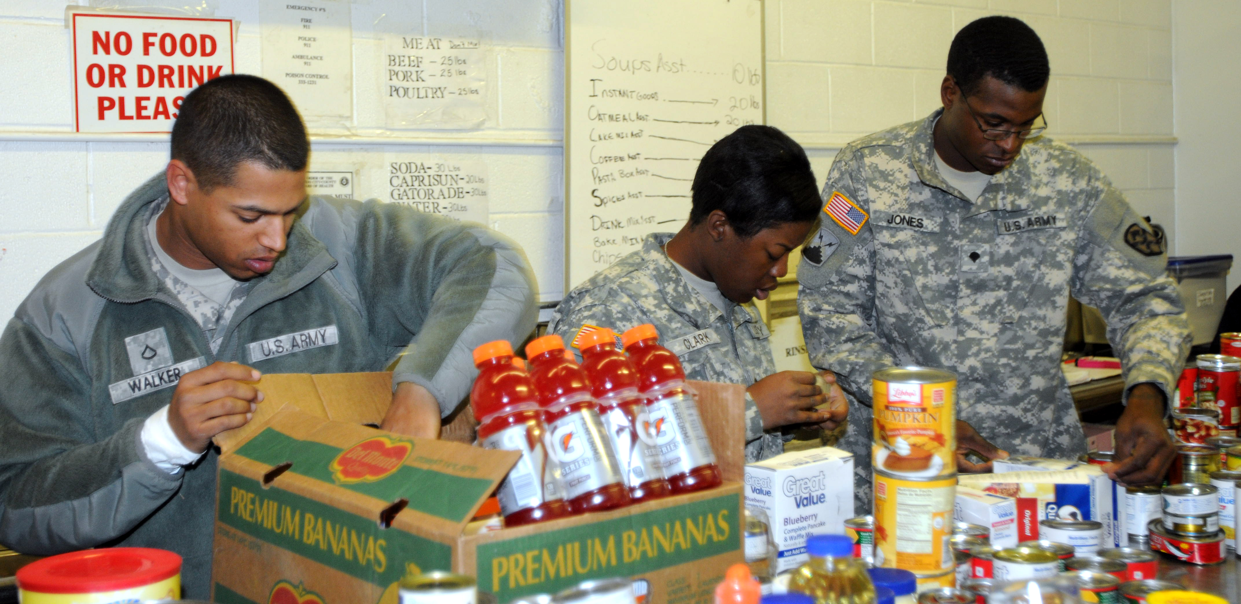 Three uniformed soldiers sort canned and packaged food at a food bank.