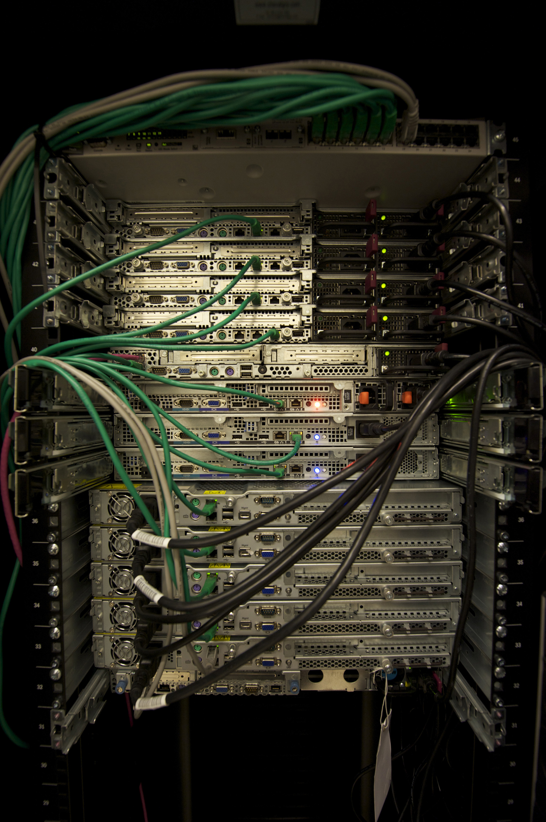 A rack of servers with green, white and dark cables connected to the rear panels.