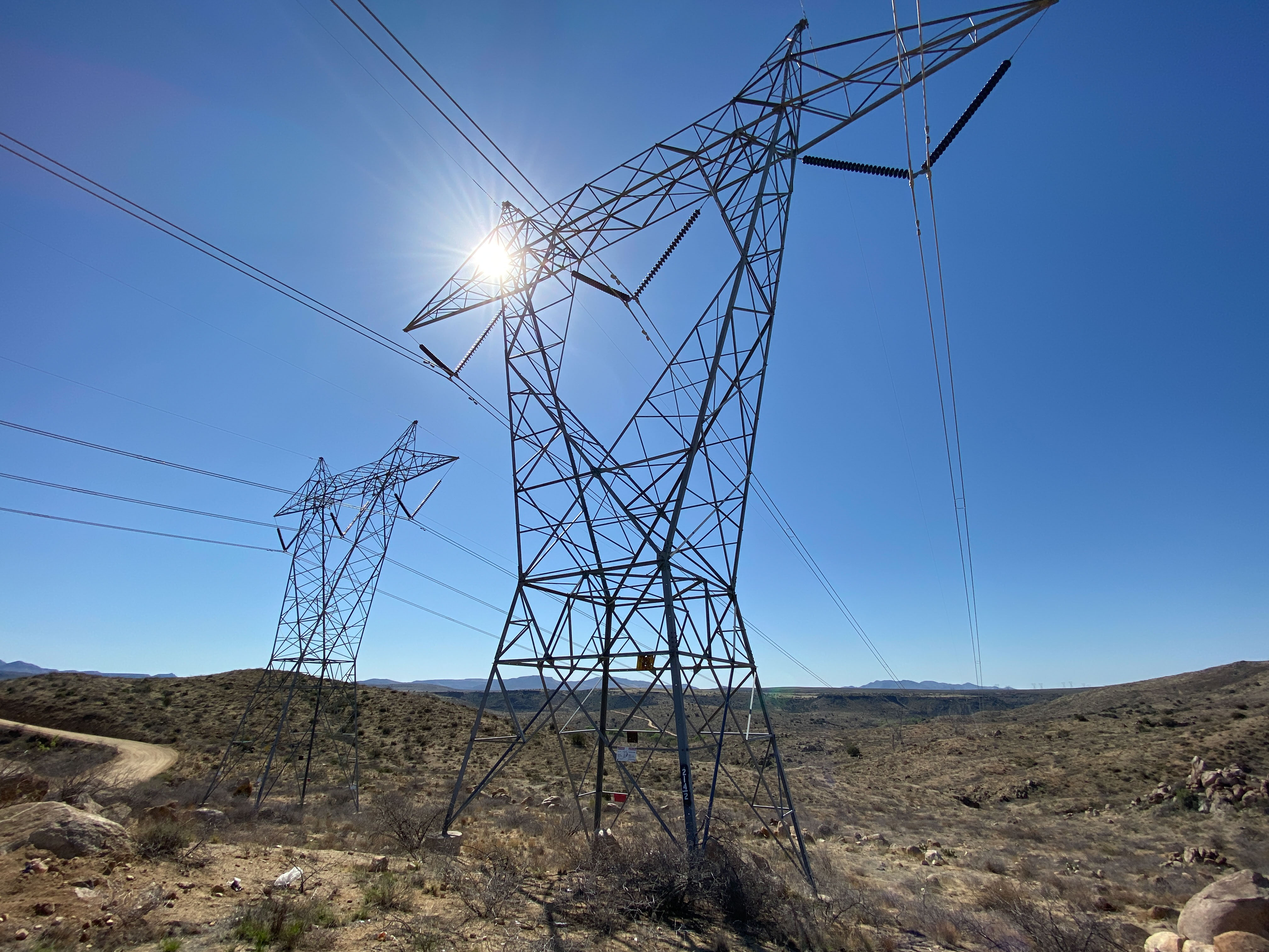 Electric transmission towers and wires across open land in Arizona.