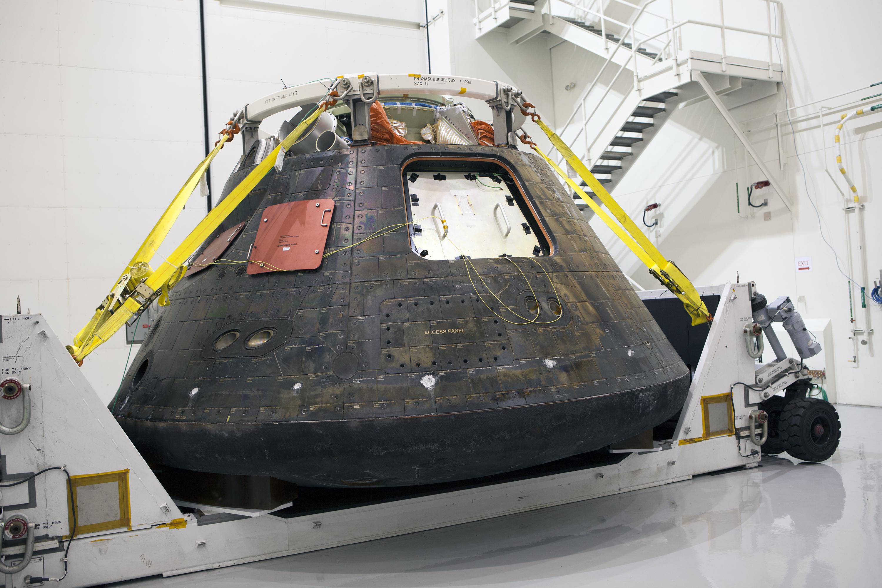 An Orion capsule suspended in lifting equipment inside a bright processing building.