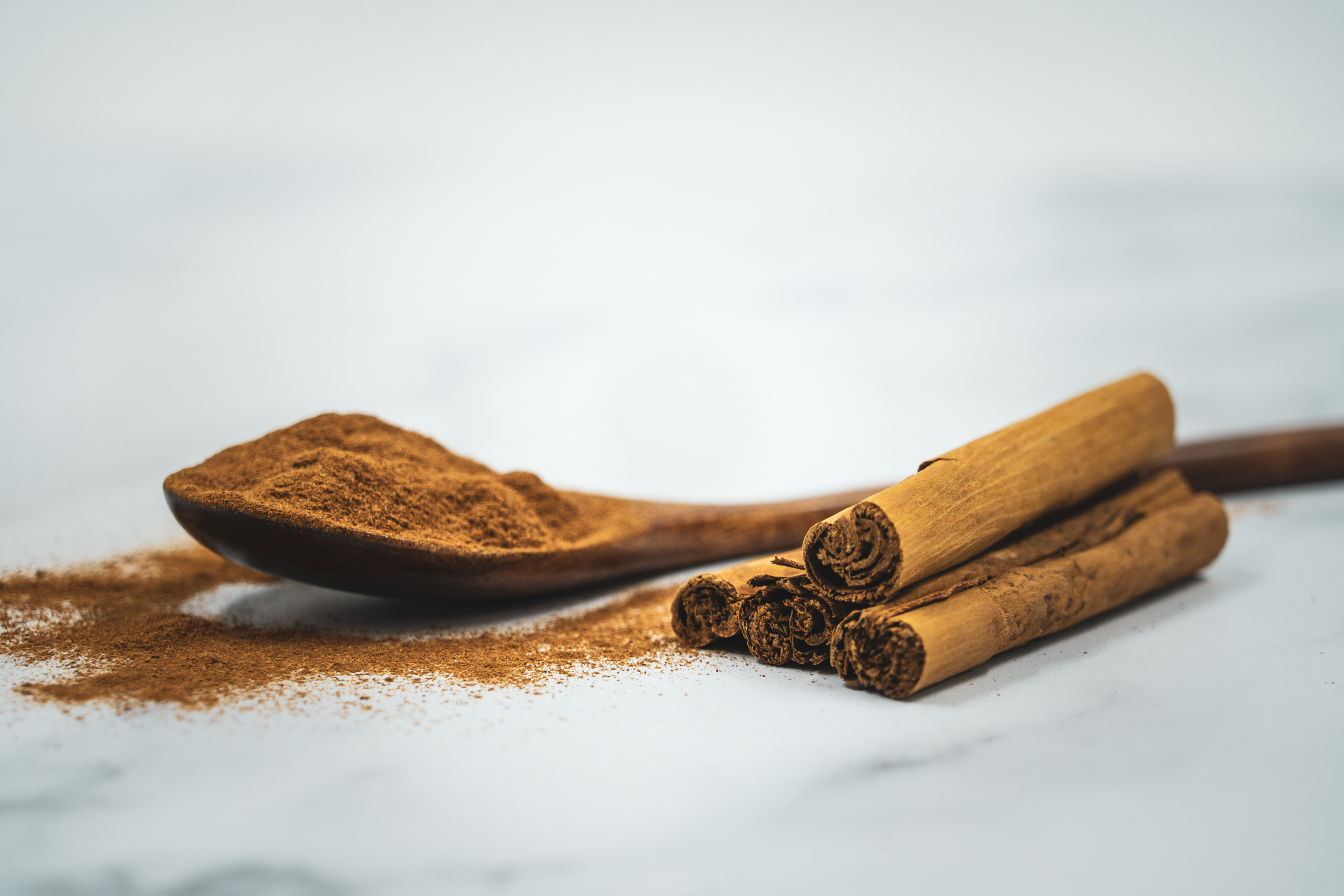 Ground cinnamon on a wooden spoon beside cinnamon sticks.